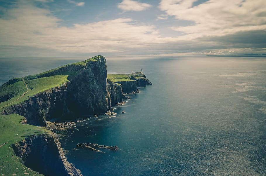 sea and rock cliff with grasses under cloudy sky, person standing in front of body of water during day time HD wallpaper