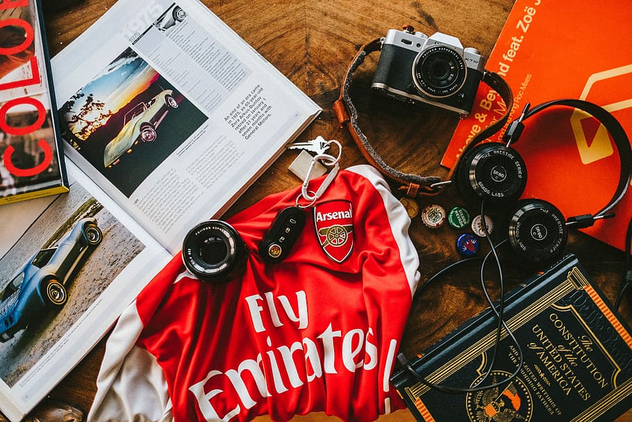 flat lay photography of soccer jersey, books, headphones, and camera, black and silver DSLR camera beside black headphones