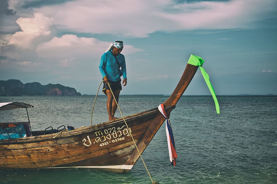 A man secures a longtail boat with rope in the Krabi district of Thailand, HD wallpaper