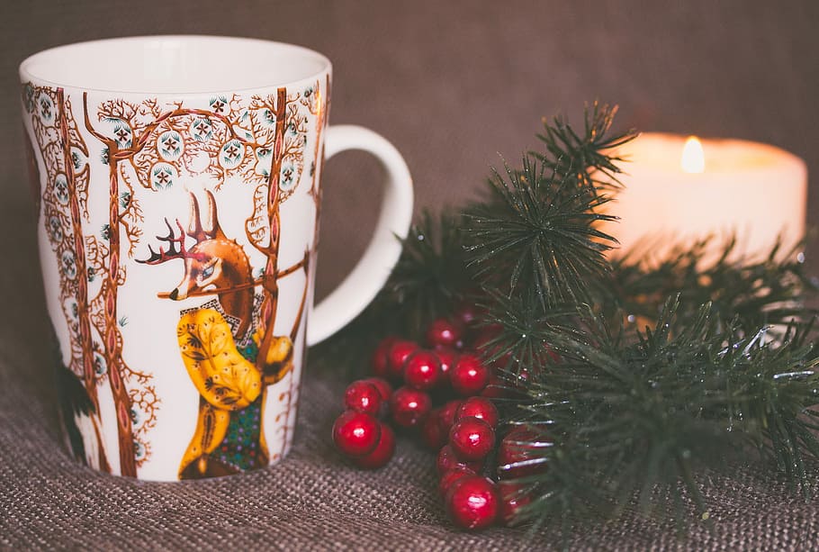 white and brown print ceramic mug near red mistletoe and candle, white and brown ceramic mug on the gray textile HD wallpaper