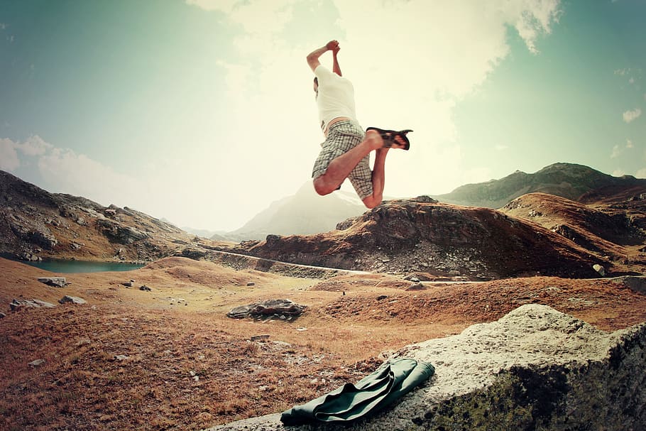 man in white shirt and gray shorts jumping over the field during daytime HD wallpaper