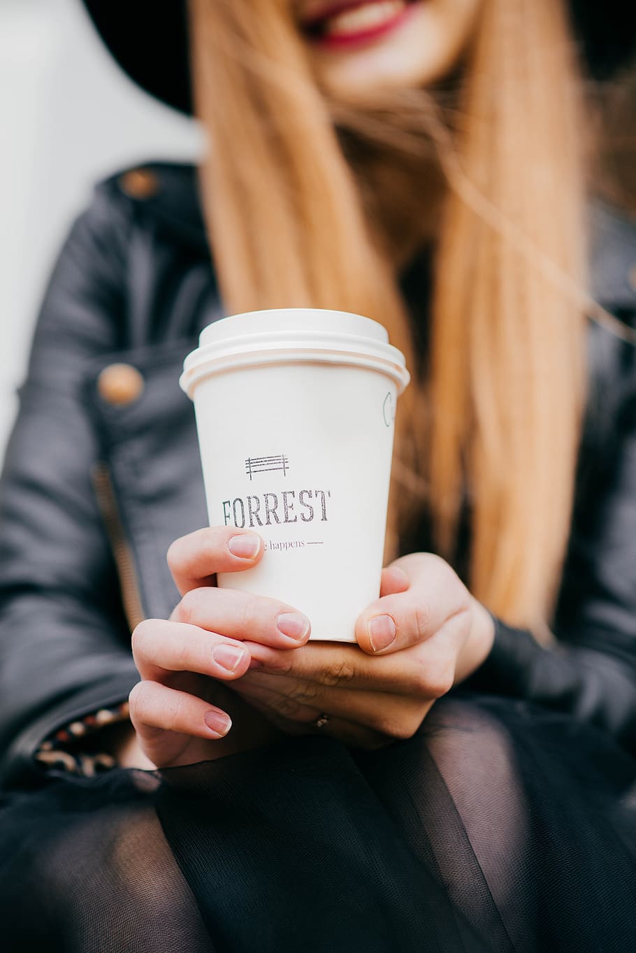 woman holding white Forrest cup with lid selective focus photography, woman wearing black leather jacket holding a Forrest print cap at daytime HD wallpaper