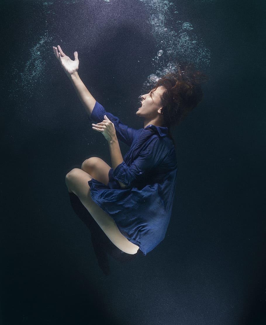 woman wearing blue elbow sleeve mini dress raising her right hand under water
