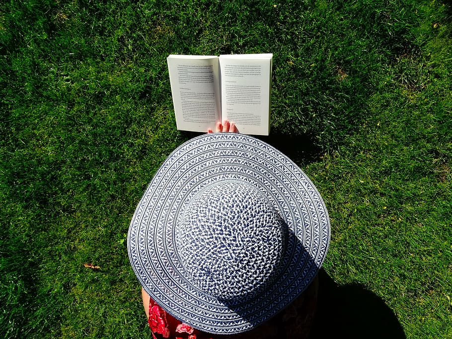 photograph of person wearing sun hat reading book on field of grass HD wallpaper