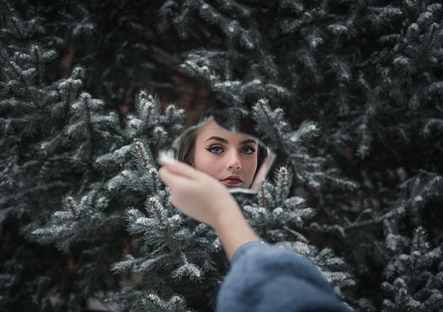 woman's face, woman in blue sweatshirt holding mirror and showing her face standing in front of pine tree with covered of snow HD wallpaper
