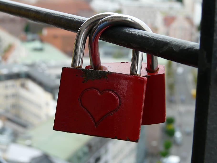 pair of red padlocks with heart engraved locked on black metal rod close-up photo