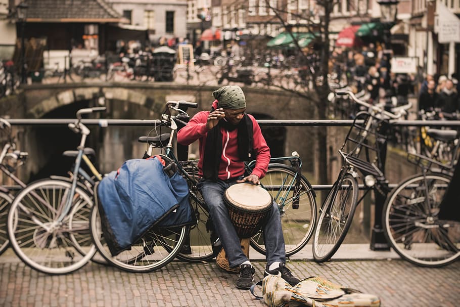 man in red shirt playing darbuka drum while sitting on gray bike near at deck rail, man in red zip-up jacket holding drum beside bridge, HD wallpaper