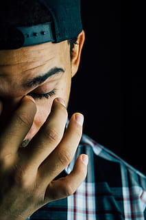 close up photo of man wearing cap and top while touching his left eye HD wallpaper