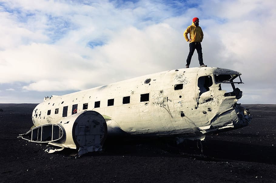man standing on white abandoned plane under white sky, man wearing yellow top on top of white steel air plane