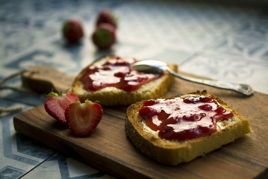 photo of bread with strawberry jam, toasted bread with strawberry jam beside sliced strawberry fruit on wooden chopping board