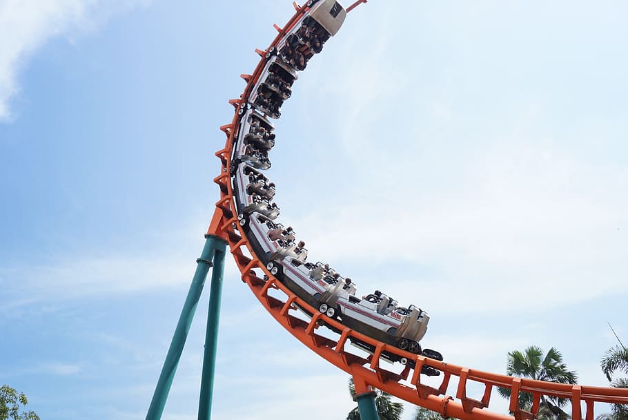people riding white and orange roller coaster under white clouds and blue sky during daytime