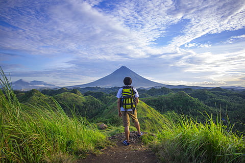 Man Wearing White Shirt, Brown Shorts, and Green Backpack Standing on Hill HD wallpaper
