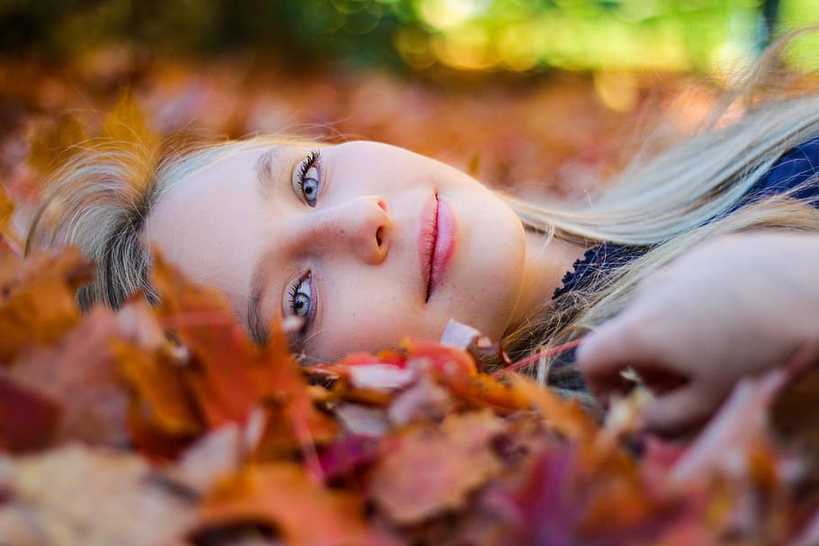 woman wearing blue top lying on dried maple leaves during daytime photography, woman lying on brown leaves, HD wallpaper
