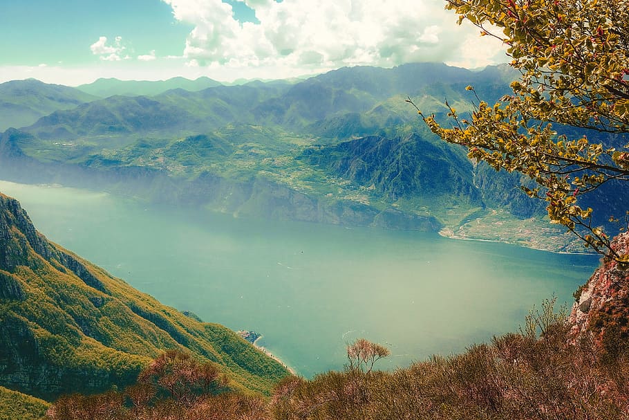 body of water surrounded with mountains, photo of lake surrounded by mountains and trees under white sky during daytime HD wallpaper