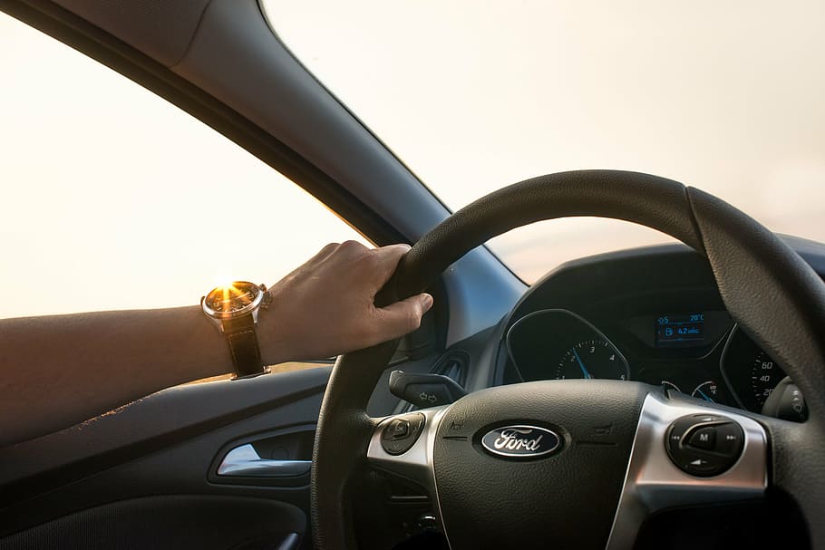 person holding gray Ford car steering wheel during daytime, driving