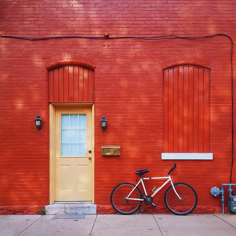 white mountain bike parked beside red painted bricked wall, house