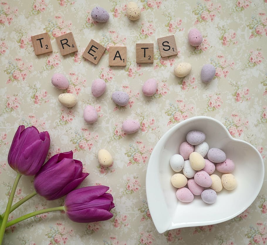 Treats scrabble letters on white, green, and pink floral surface beside chocolate eggs and heart-shaped white ceramic bowl, HD wallpaper