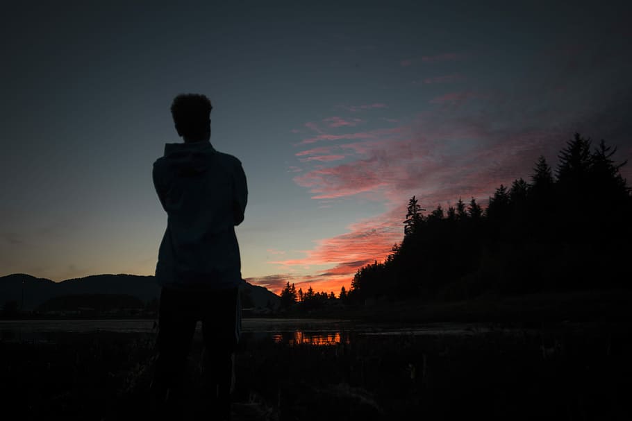 silhouette photography of person standing in front of lake, person standing near fire pit under golden hour silhouette HD wallpaper
