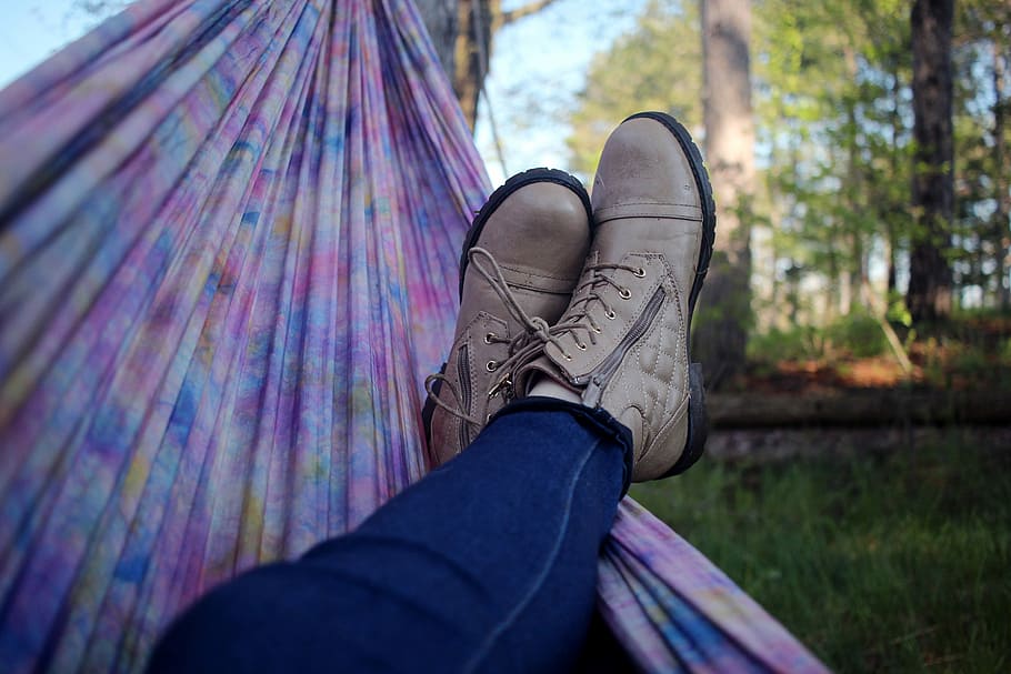 person lying on pink and purple hammock surrounded with trees, person wearing pair of brown boots, HD wallpaper