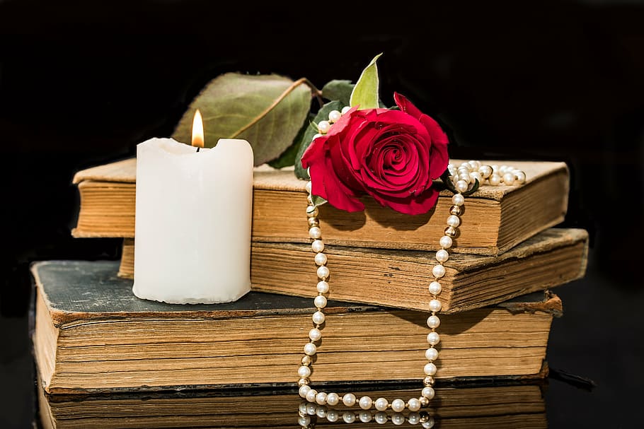 white candle near red rose, old books, pearl necklace, blossom