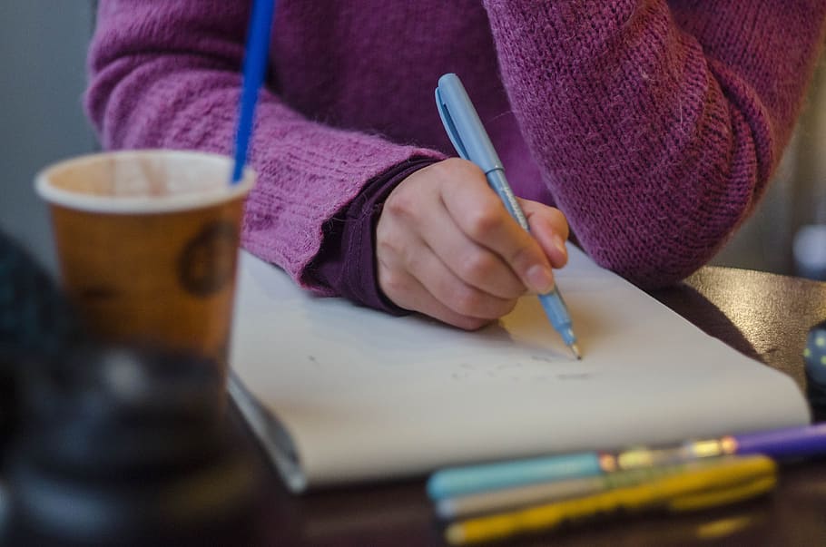 selective focus photography of person holding pen writing on paper on table near coffee cup HD wallpaper