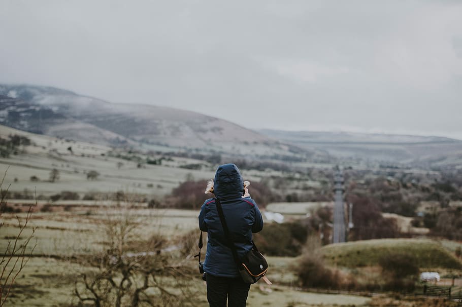 Woman photographing valley, selective focus photography of person in hooded jacket looking at trees and mountains HD wallpaper