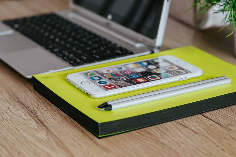 Silver Acer laptop, a white Apple iPhone and a notepad on a wooden desk HD wallpaper