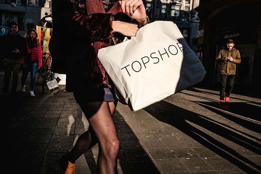 woman carrying white TopShop paper bag near man wearing brown jacket, person holding white Topshoe bag, HD wallpaper