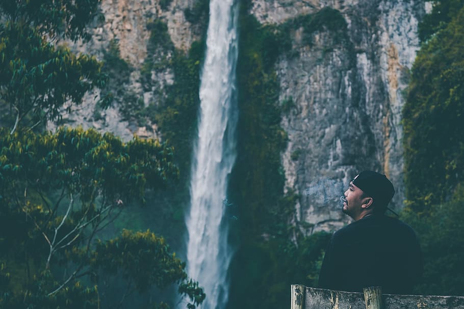 man standing near falls during daytime, man sitting in front of waterfalls HD wallpaper
