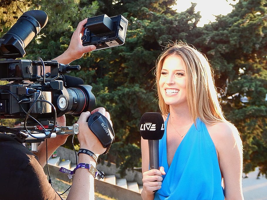 woman smiling while holding a microphone, reporter, camera, journalist