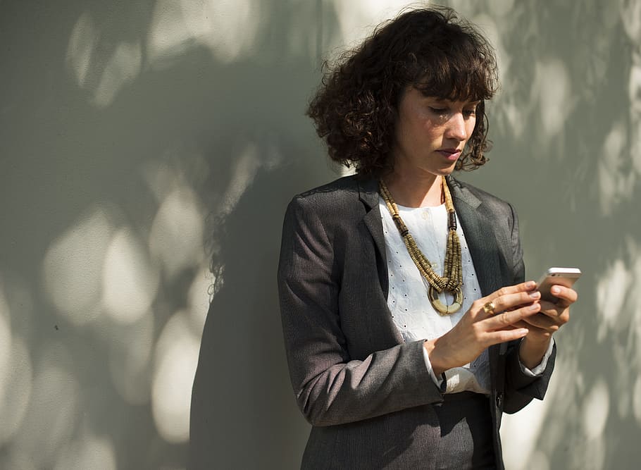 woman holding phone while standing beside wall, networking HD wallpaper