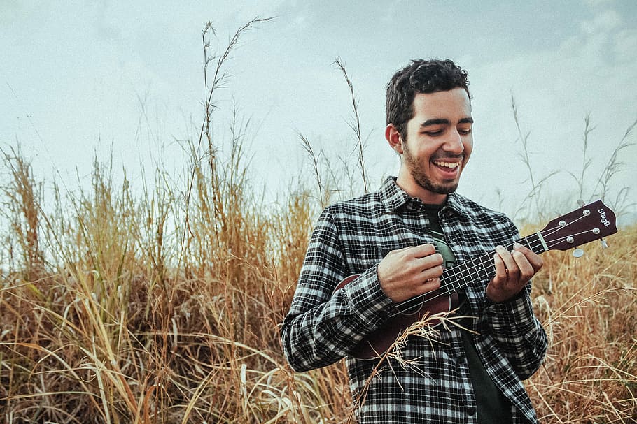 man playing ukulele while standing on grass field, man standing on dried grass playing ukulele HD wallpaper