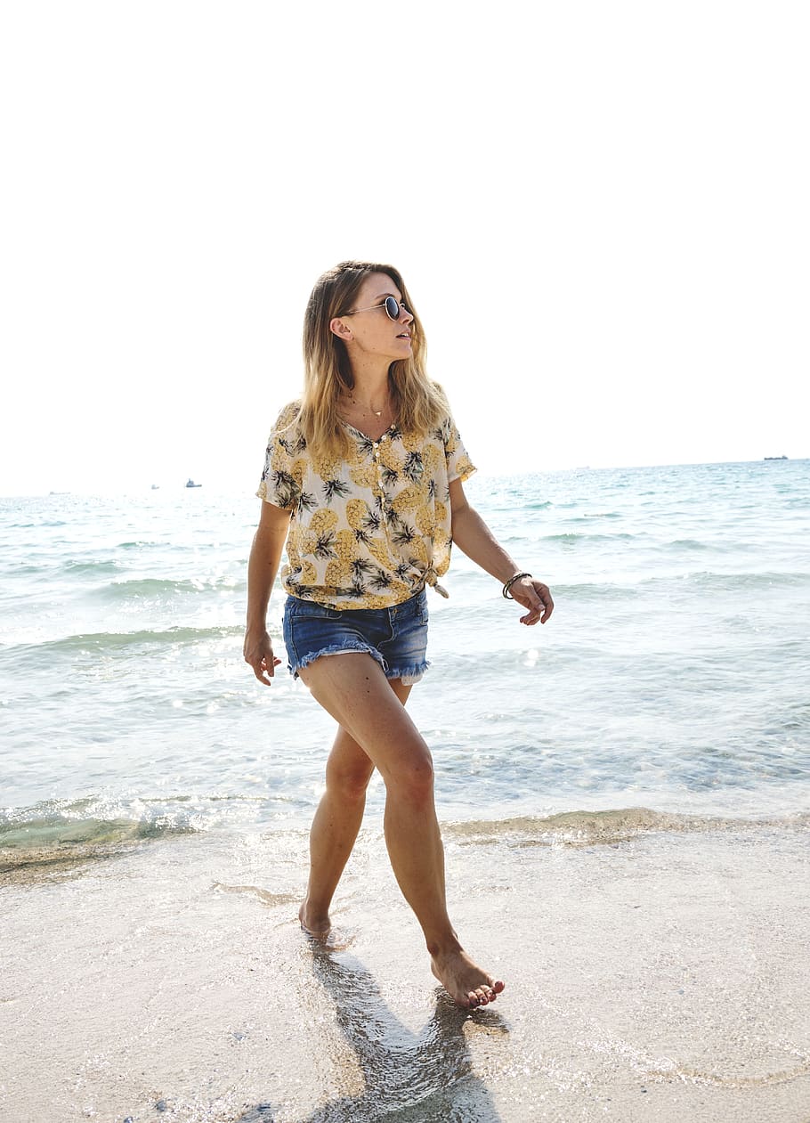 woman wearing beige pineapple print shirt walking on seashore