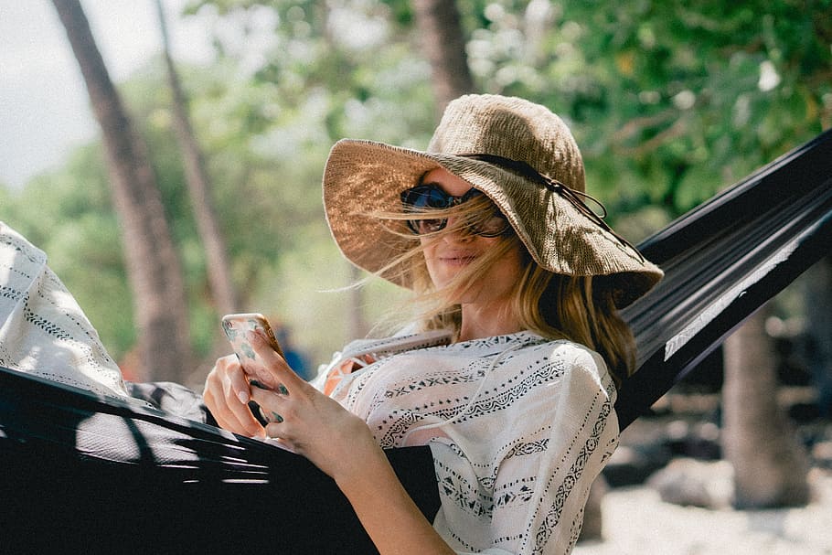woman lying on black hammock while holding phone, woman lies on hammock outdoor during day HD wallpaper