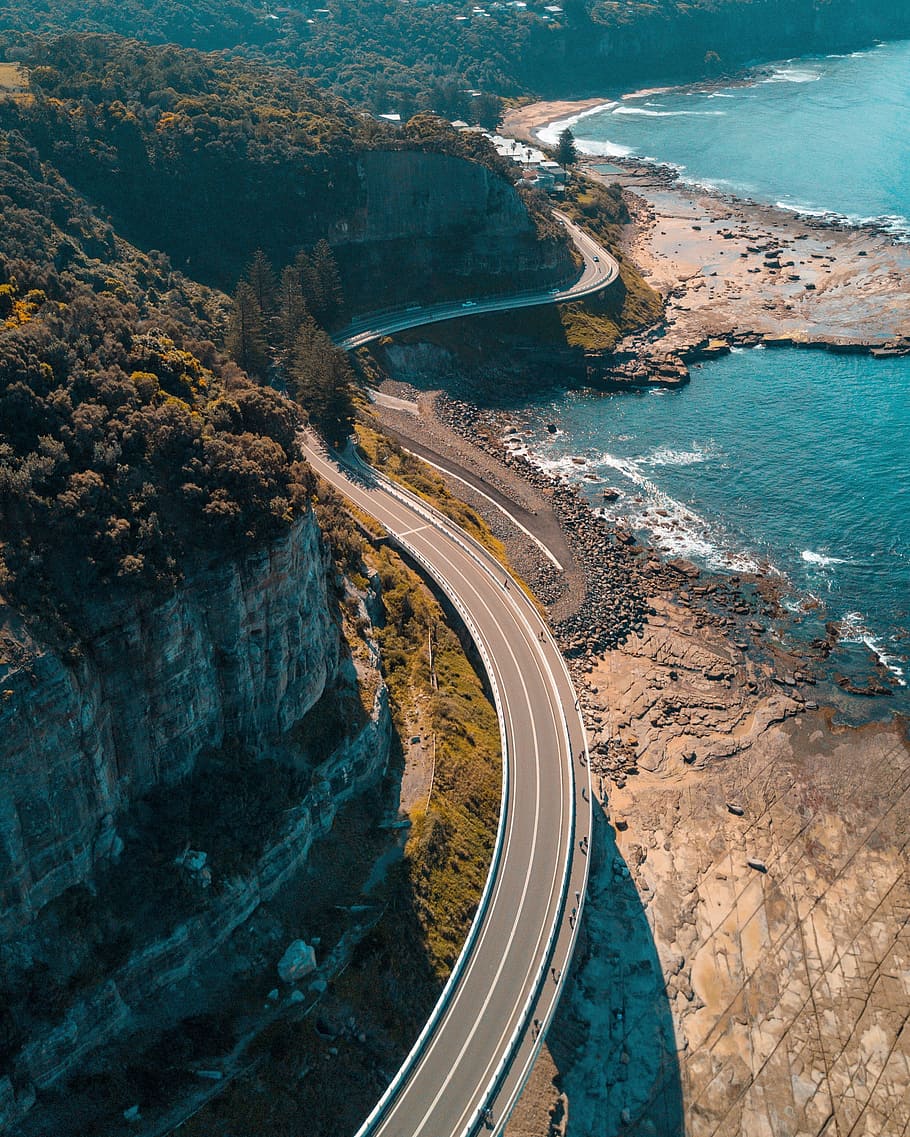 birds eye view of highway beside bay, concrete road beside cliff near body of water at daytime HD wallpaper