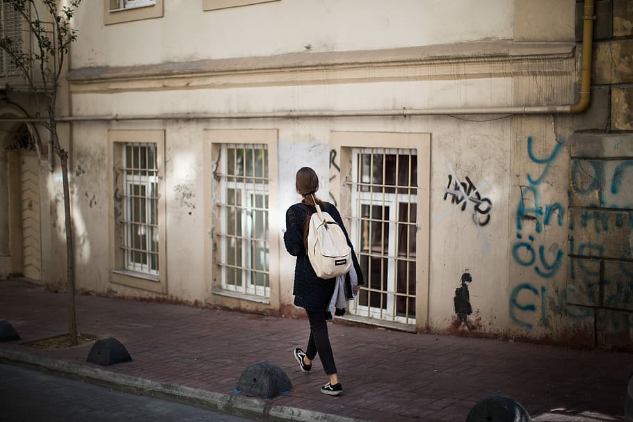 woman walking on sidewalk nearby beige structure, woman walking beside concrete building