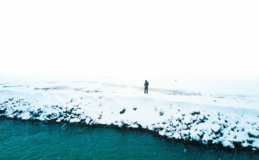 man standing at snowfield near body of water, person standing on snowy ground beside body of water HD wallpaper