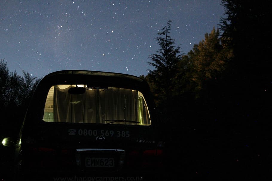 black vehicle parked near trees during nighttime, van under starry sky