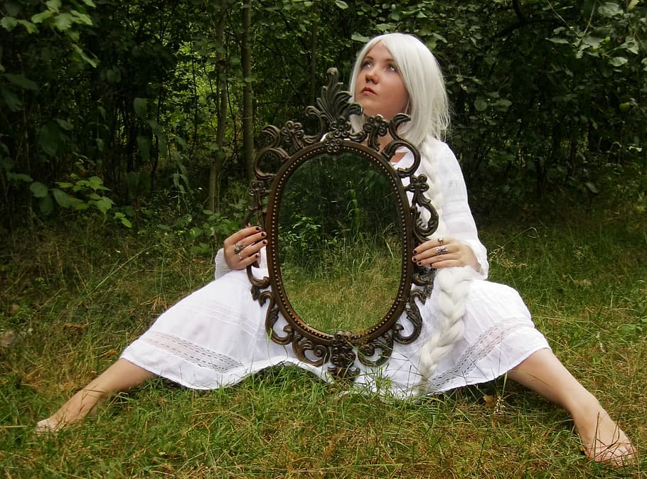woman wearing white dress holding mirror while sitting on grass at daytime HD wallpaper