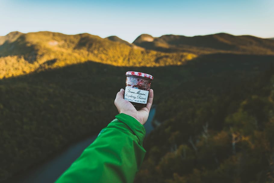 person holding clear glass jar with cap near mountain, person wearing green long-sleeved top and holding white jar HD wallpaper