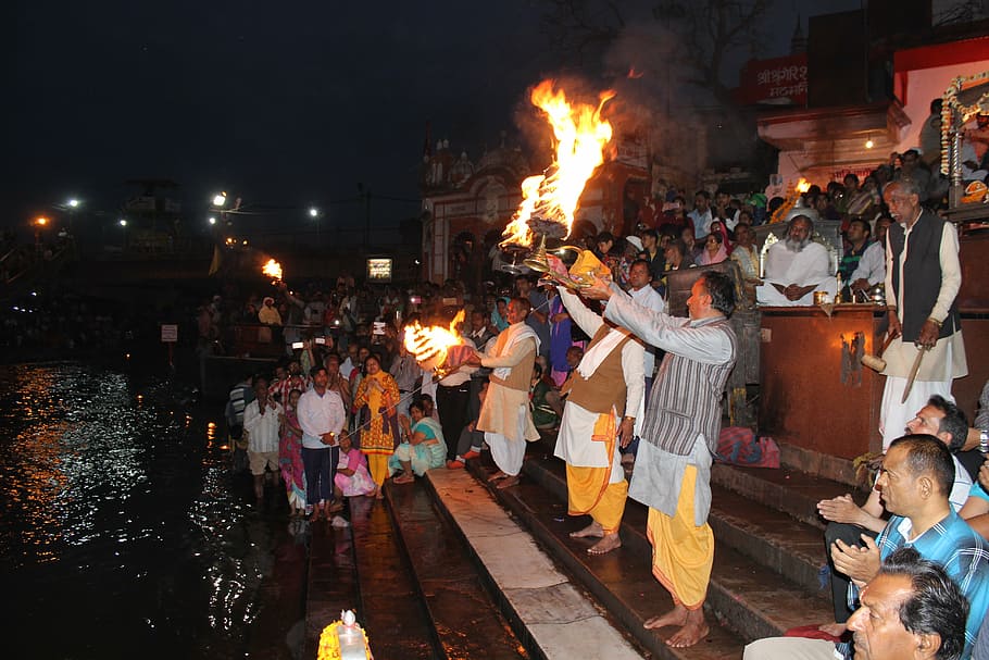 man holding fire beside crown of people near body of water, aarti