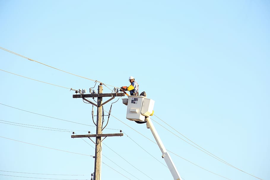 man standing on bucket beside gray current post at daytime, person standing inside the boom beisde electric post HD wallpaper