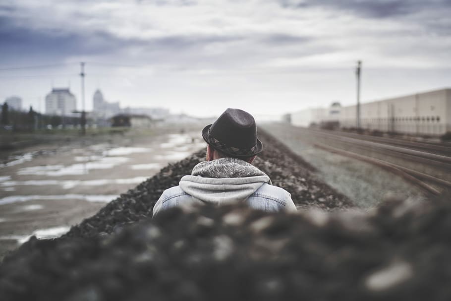 selective focus of man sitting beside body of water, shallow focus photography of man wearing black fedora hat HD wallpaper