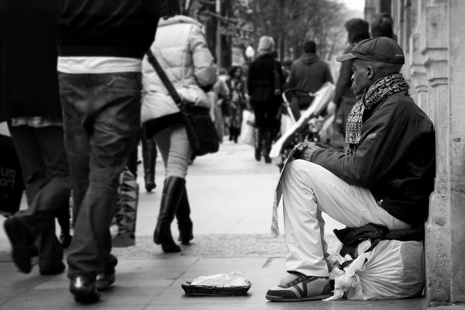 man sitting down on white seat near building looking at people passing by HD wallpaper