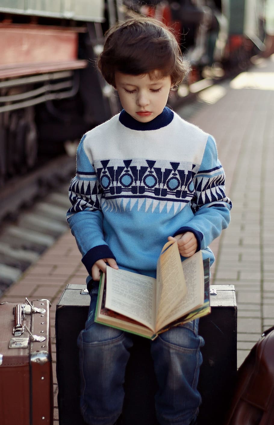boy wearing multicolored sweater reading and holding book on lap HD wallpaper