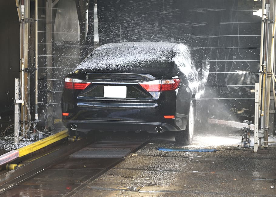 black sedan being washed in a moving car wash during day, clean