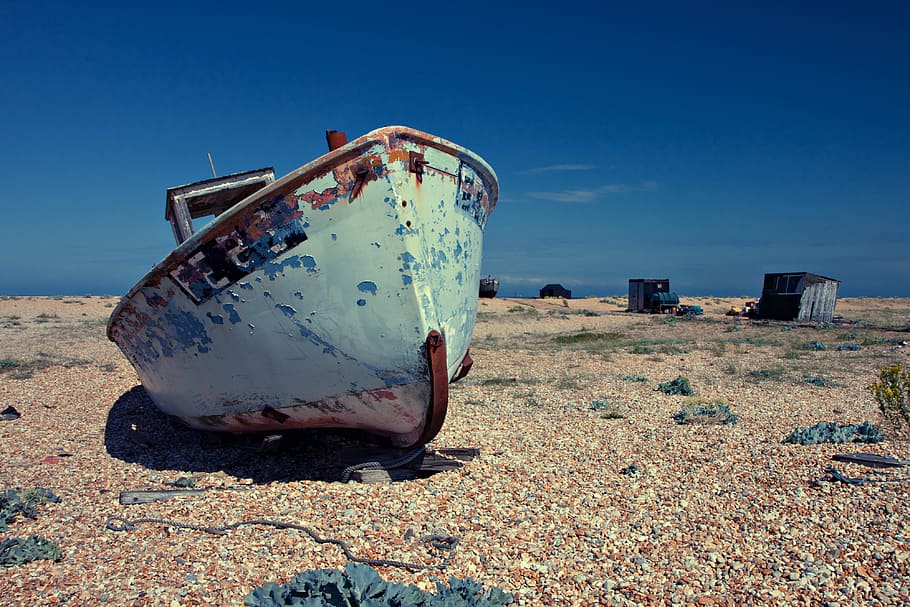 An old abandoned boat lies on a shingle beach on a sunny day. Image captured in Dungeness, Kent, England HD wallpaper