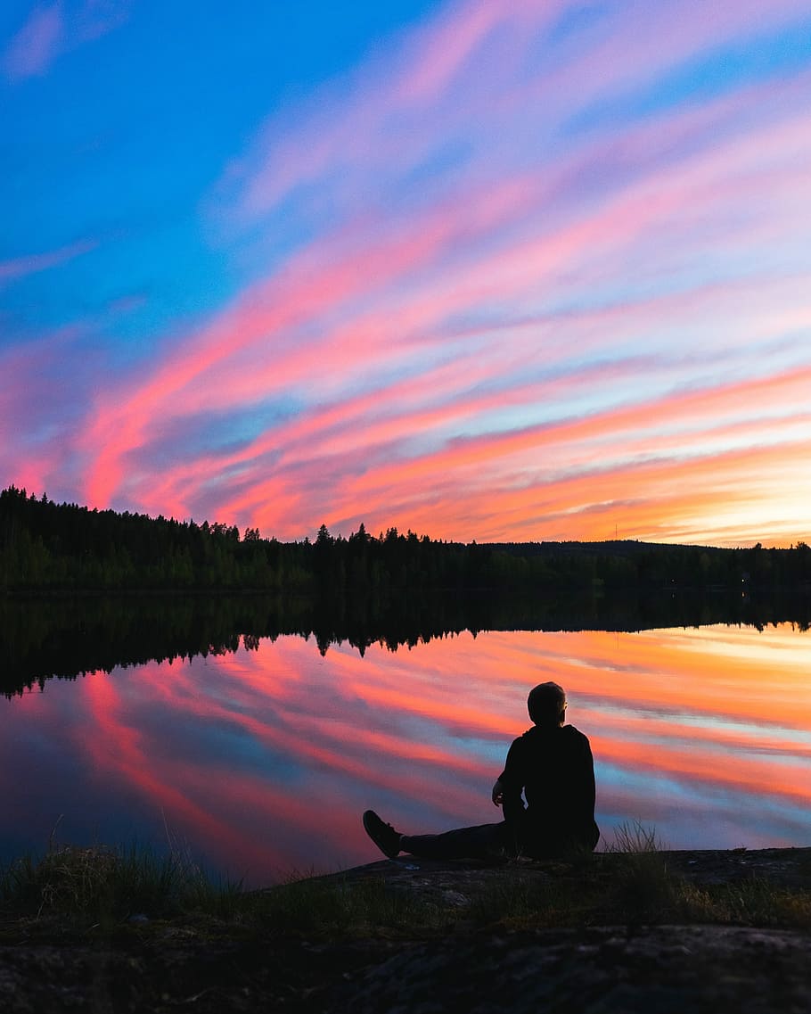 silhouette of man sitting on water's edge facing mountain during golden hour, silhouette of person sitting in front of lake during daytime HD wallpaper