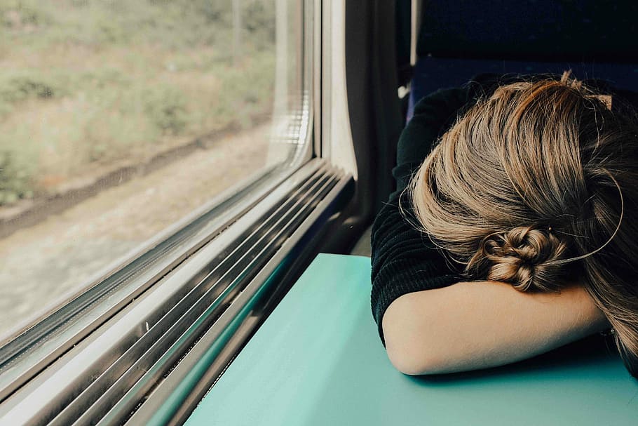 sleeping woman in train at daytime, woman leaning on teal table inside vehicle near clear glass window
