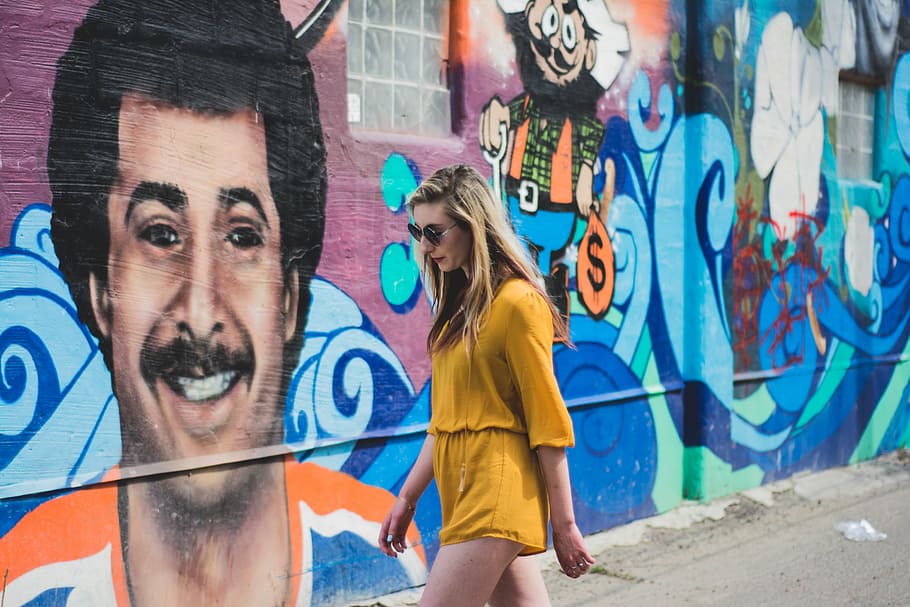 woman walking beside wall with graffiti, wearing, yellow, romper